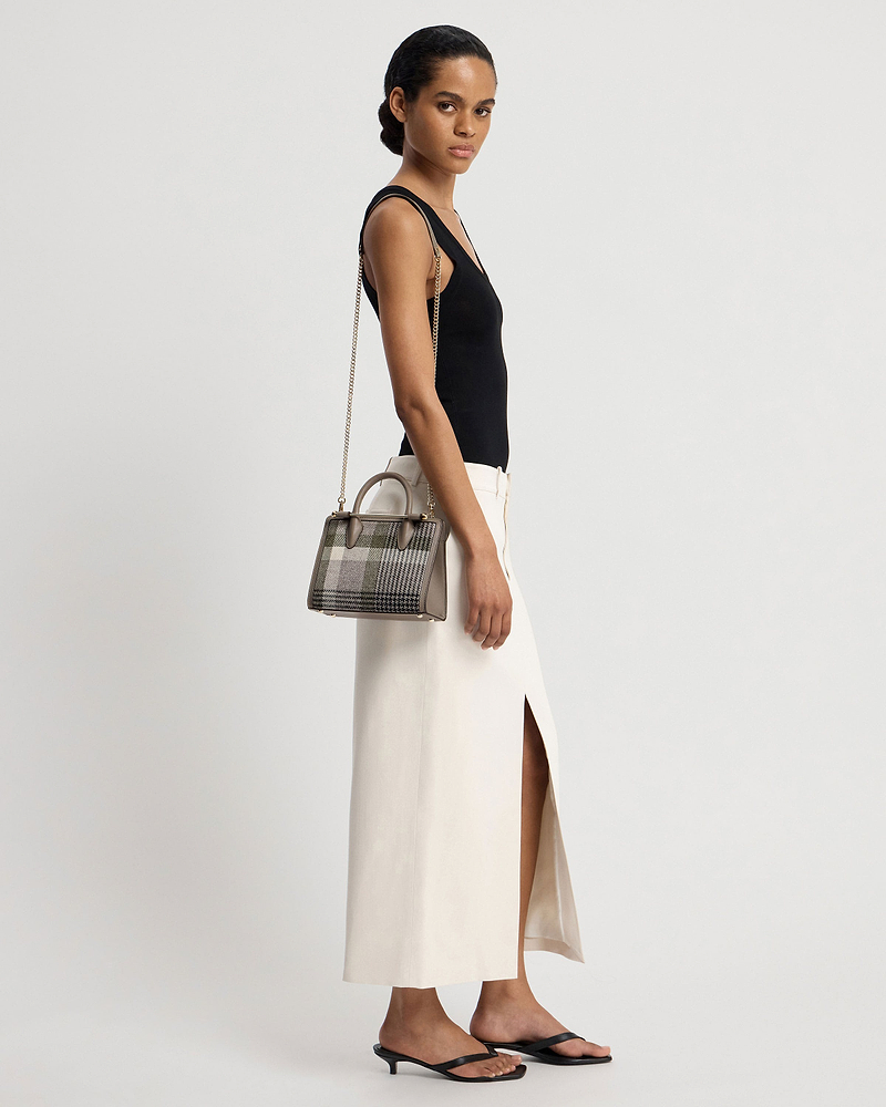 Model wearing black top and cream skirt carrying a tartan taupe mini tote.