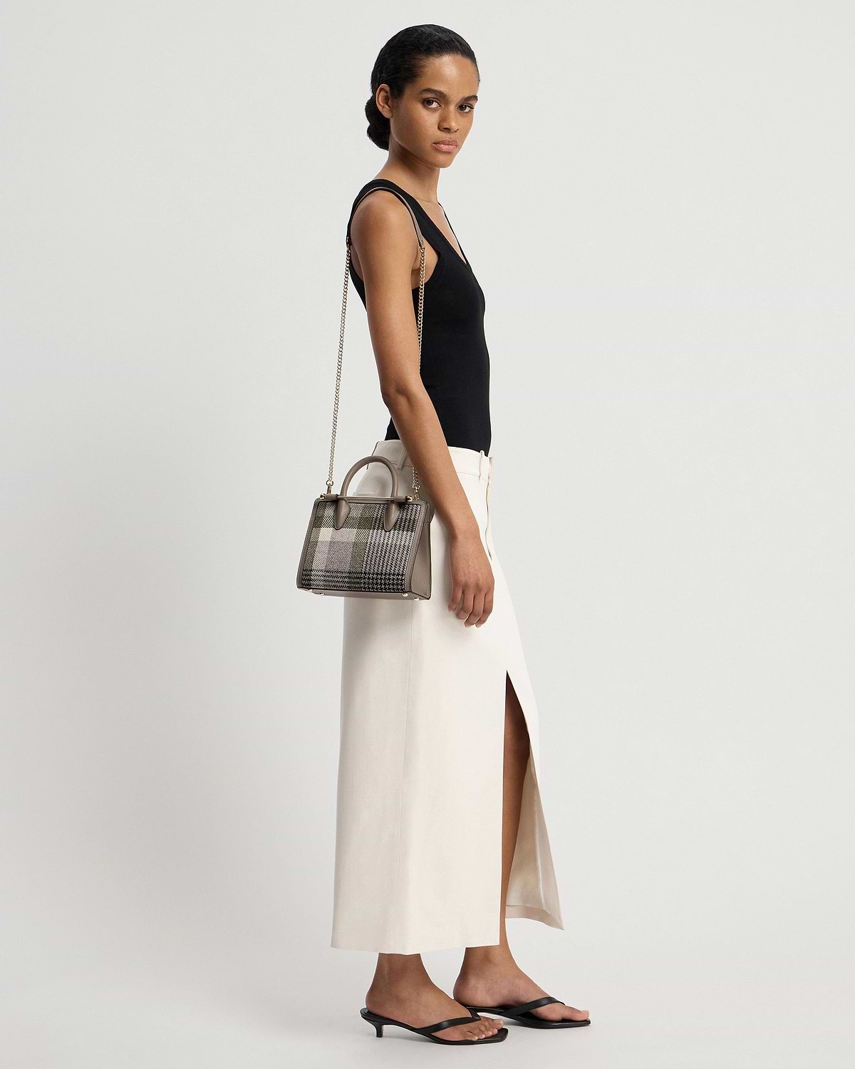 Model wearing black top and cream skirt carrying a tartan taupe mini tote.