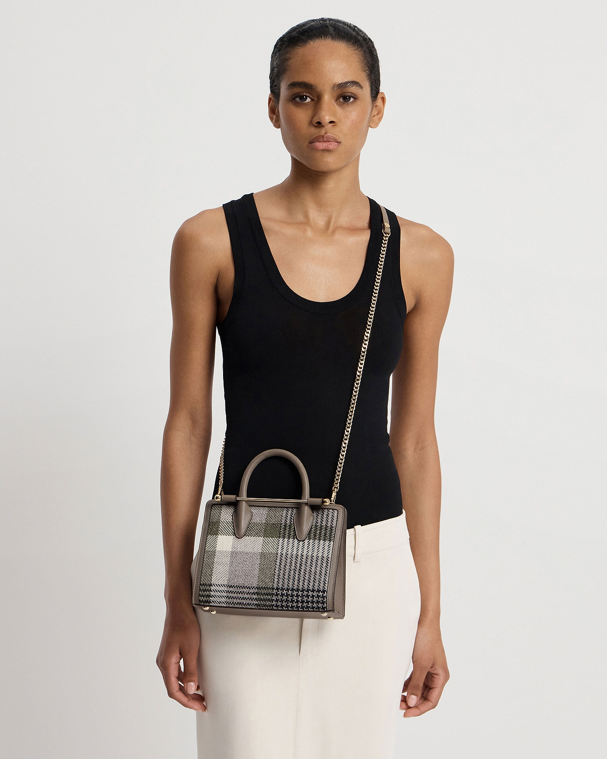 Model wearing black tank top holding tartan taupe mini tote with chain strap