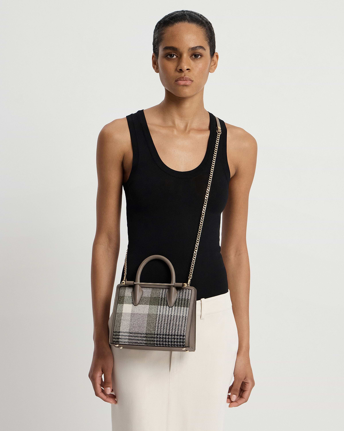 Model wearing black tank top holding tartan taupe mini tote with chain strap