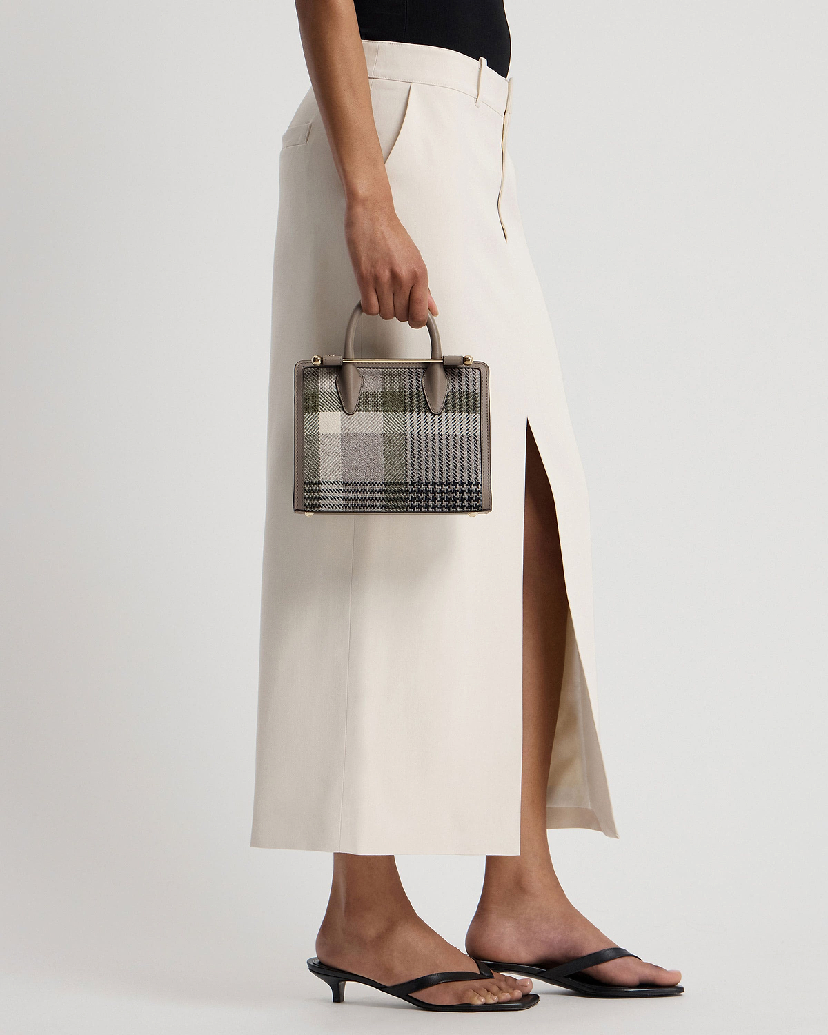 Model holding a taupe tartan mini tote by the top handle at their side