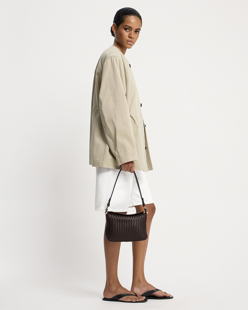 Model in beige jacket holding chocolate woven leather shoulder bag.