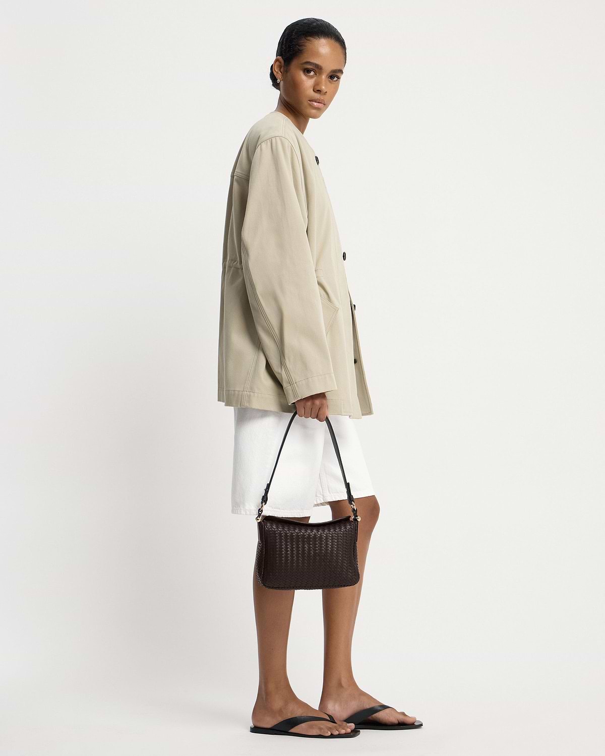 Model in beige jacket holding chocolate woven leather shoulder bag.
