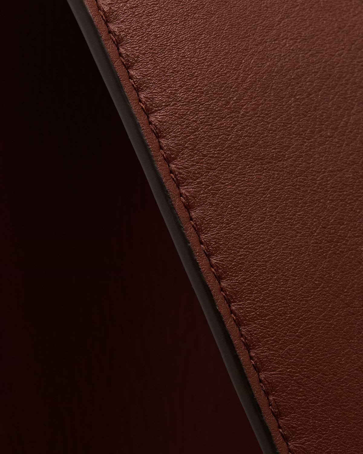 Walnut leather tote edge showing visible stitching and textured surface.