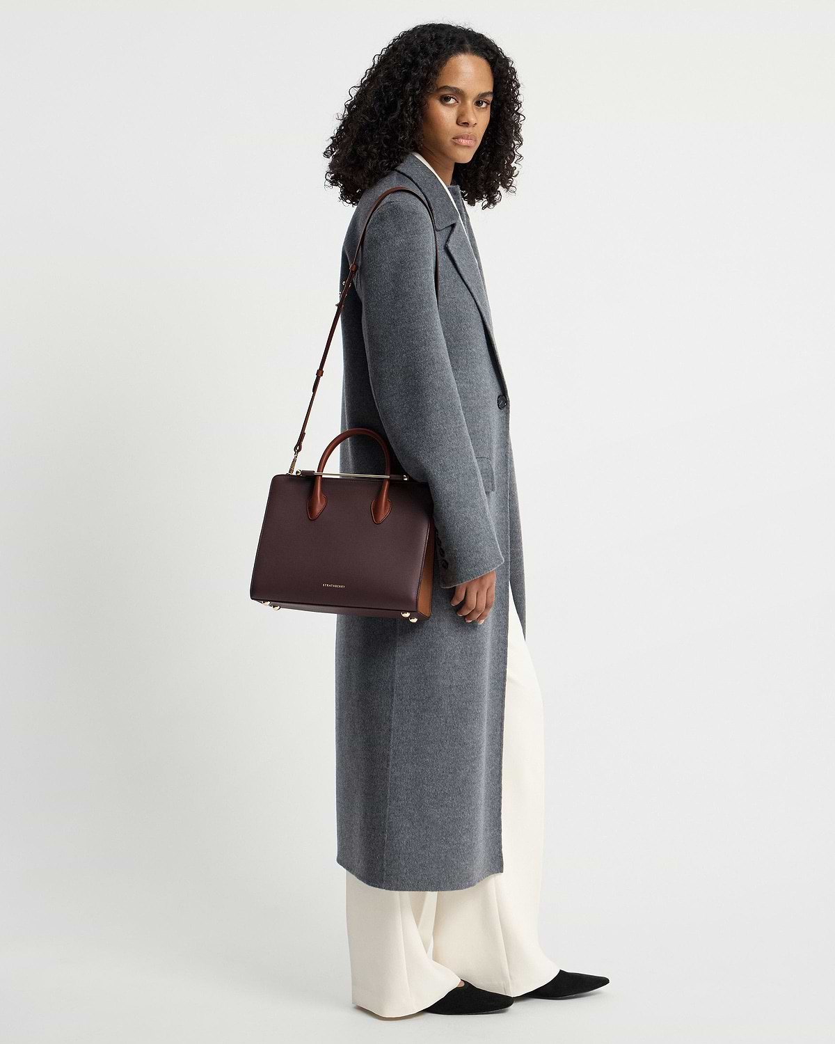 Model in grey long coat carrying Strathberry burgundy, walnut and chestnut midi tote.