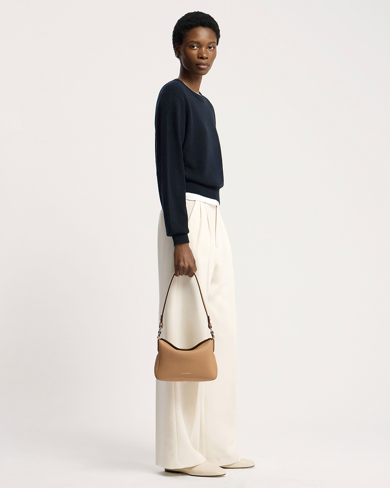 Model holding a caramel Strathberry Sway shoulder bag with top handle and visible logo.
