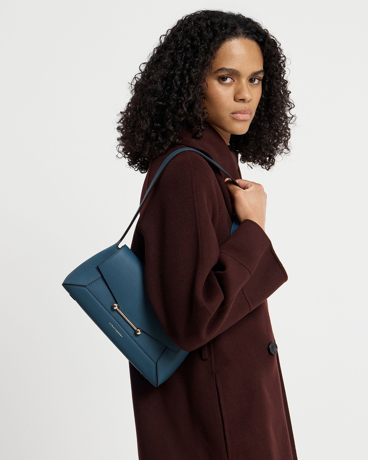 Model wearing burgundy coat holding Strathberry Mosaic Shoulder bag in Loch Blue