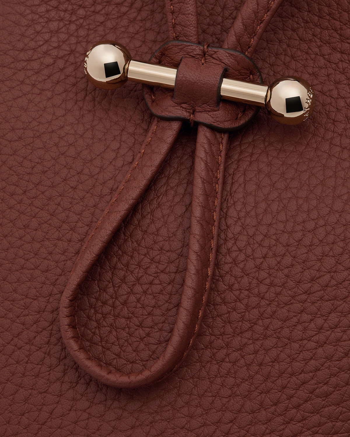 Pebbled walnut leather surface with drawstring cords and gold bar toggle fastener.