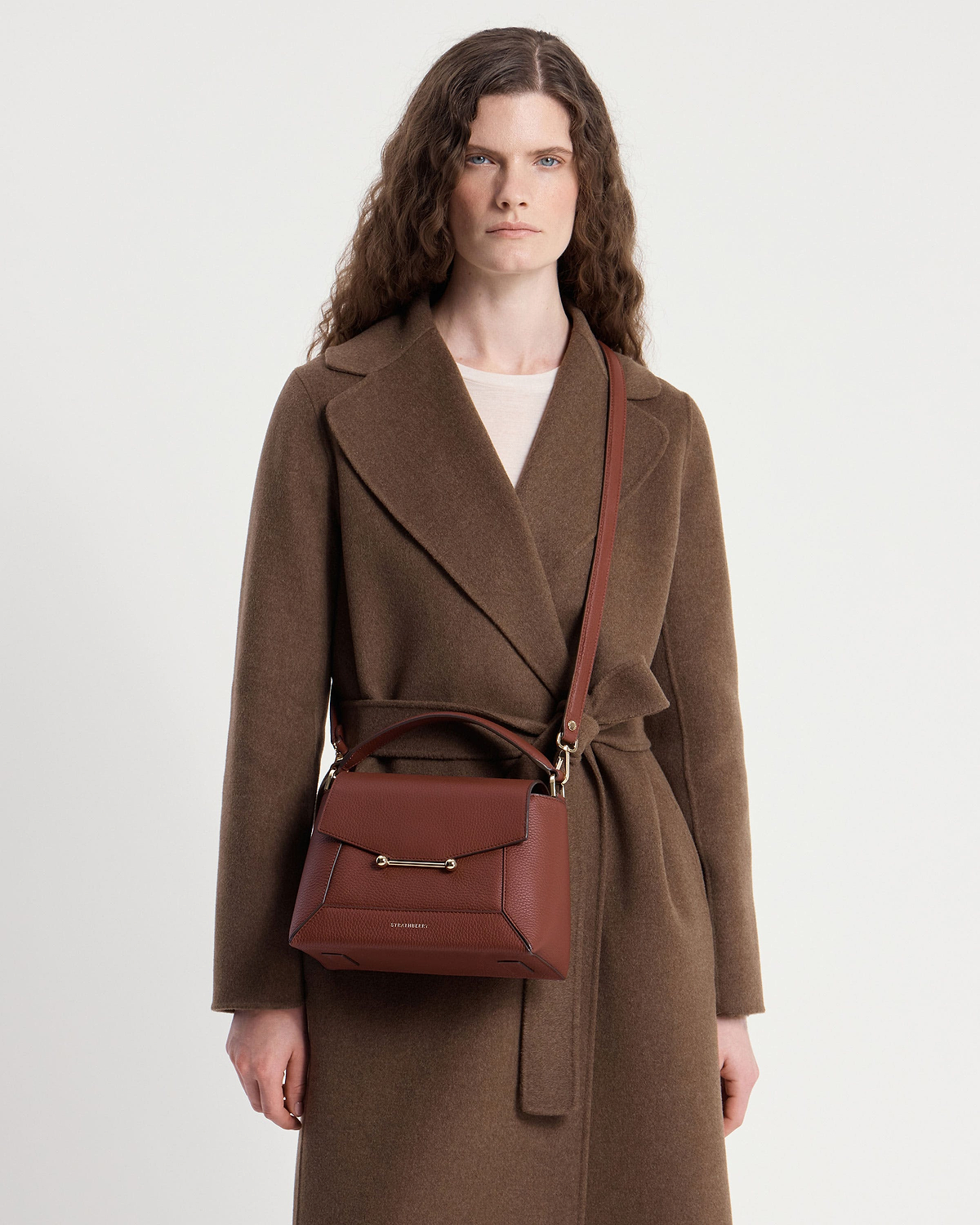 Model wearing brown coat with walnut mosaic crossbody bag, visible gold hardware.