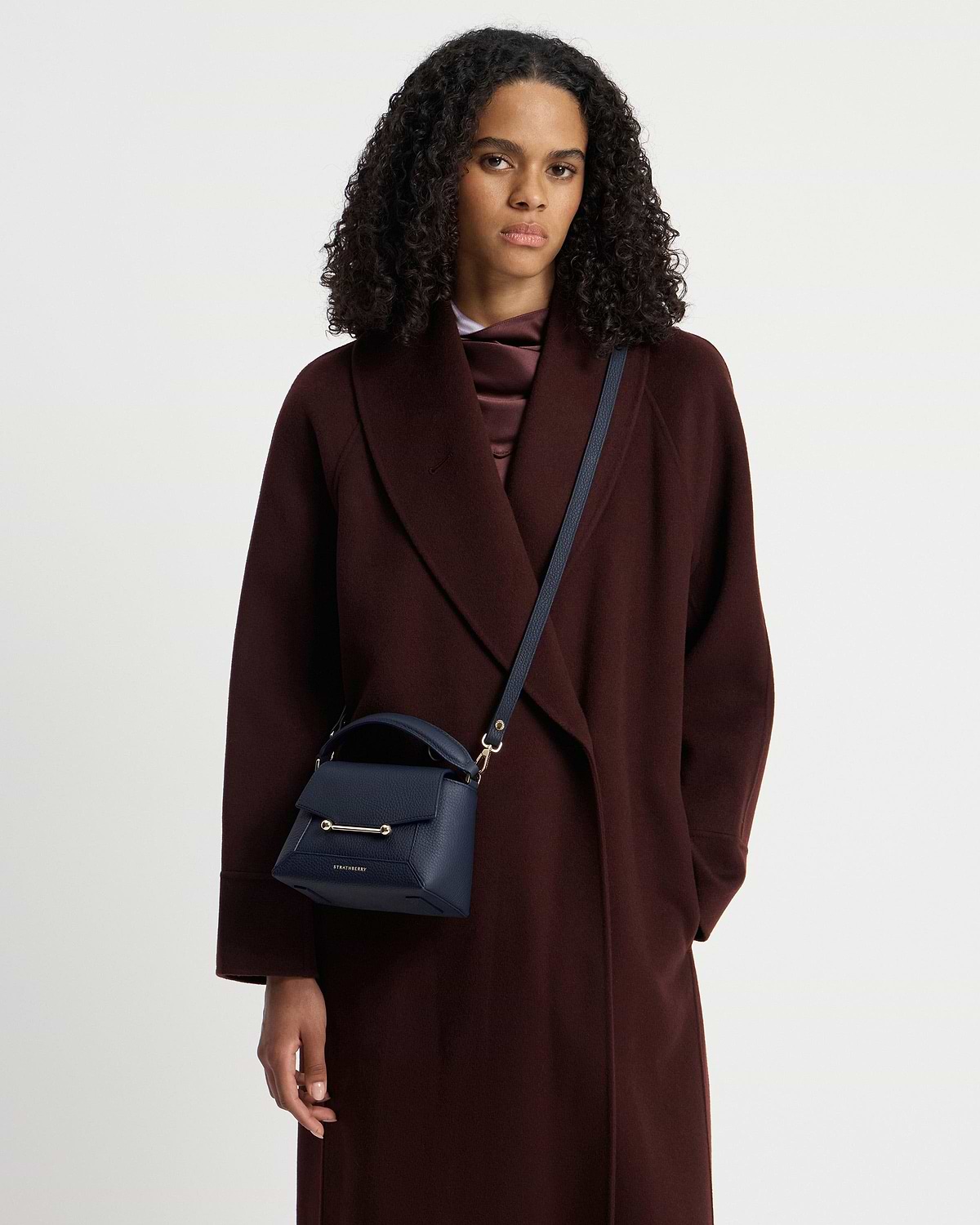 Model wearing navy Strathberry Mosaic Nano crossbody bag over a dark coat
