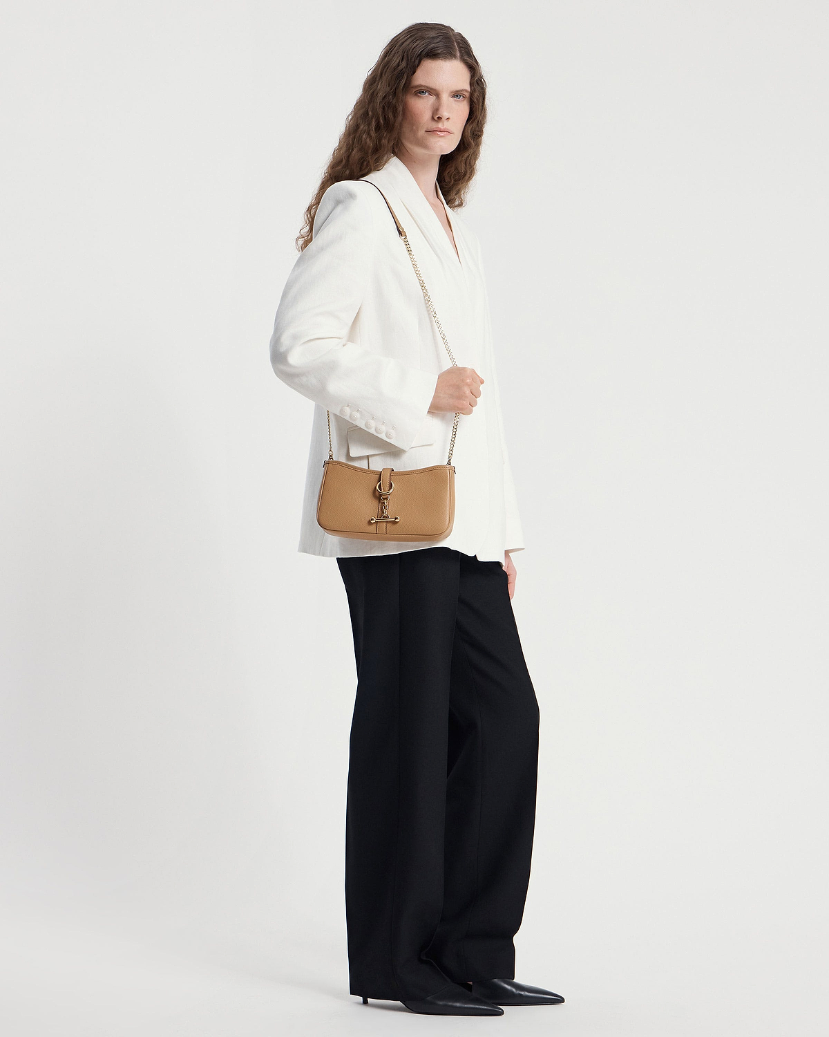 Caramel leather shoulder bag with gold chain strap worn by model in white blazer.