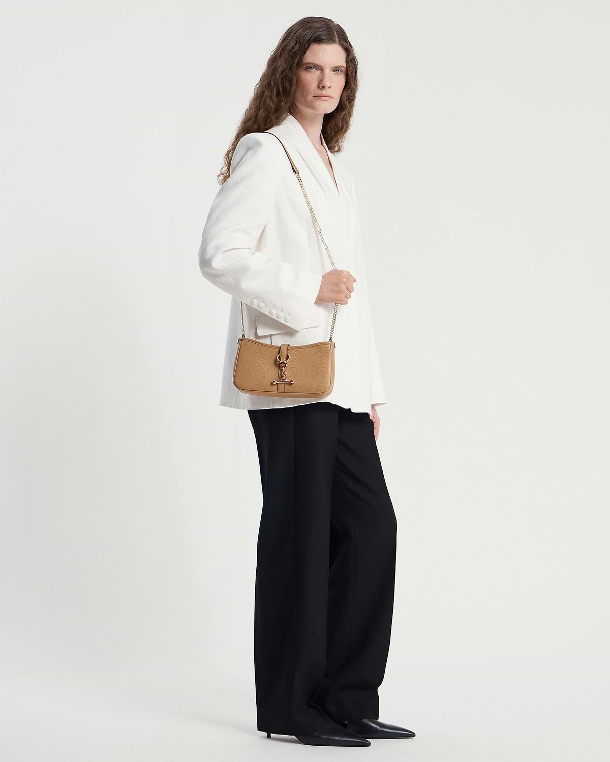 Caramel leather shoulder bag with gold chain strap worn by model in white blazer.