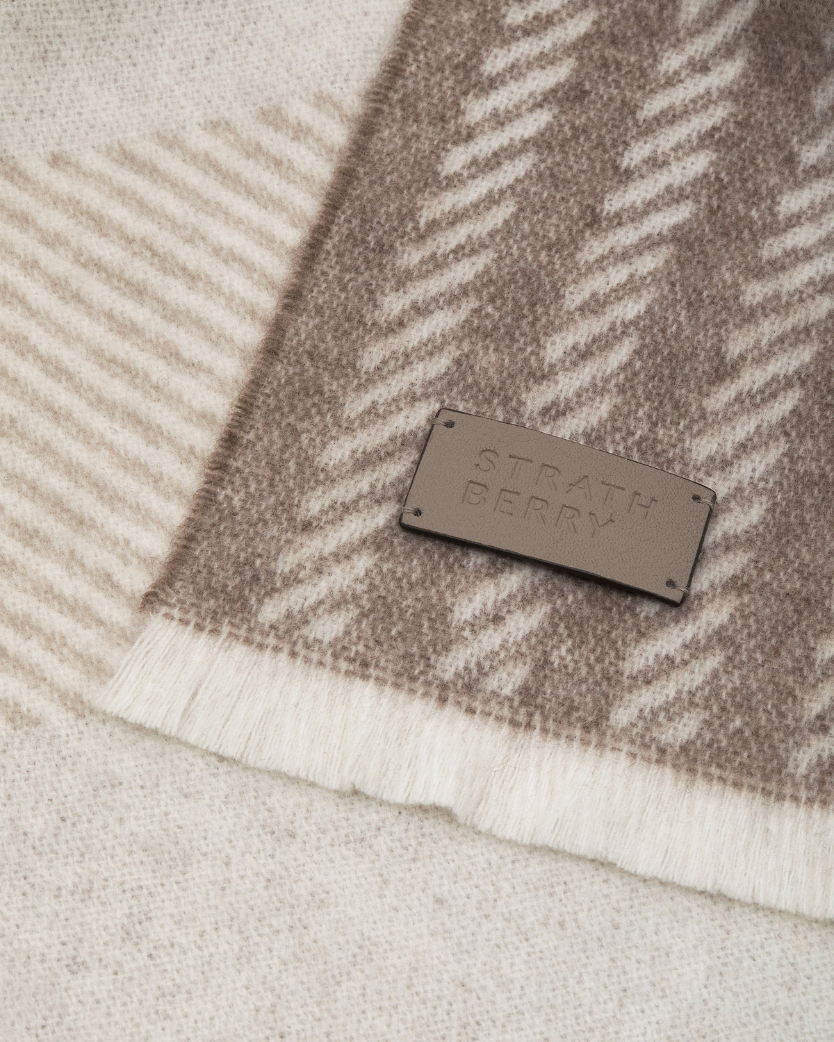 Taupe tartan cashmere scarf showing texture and Strathberry leather label.