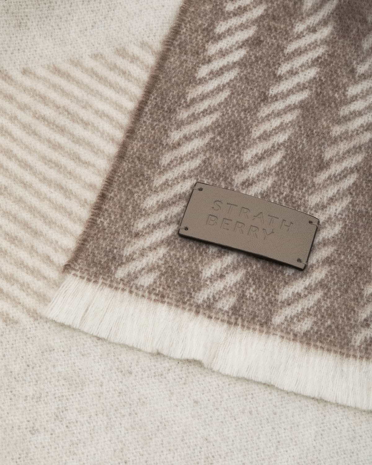 Taupe tartan cashmere scarf showing texture and Strathberry leather label.