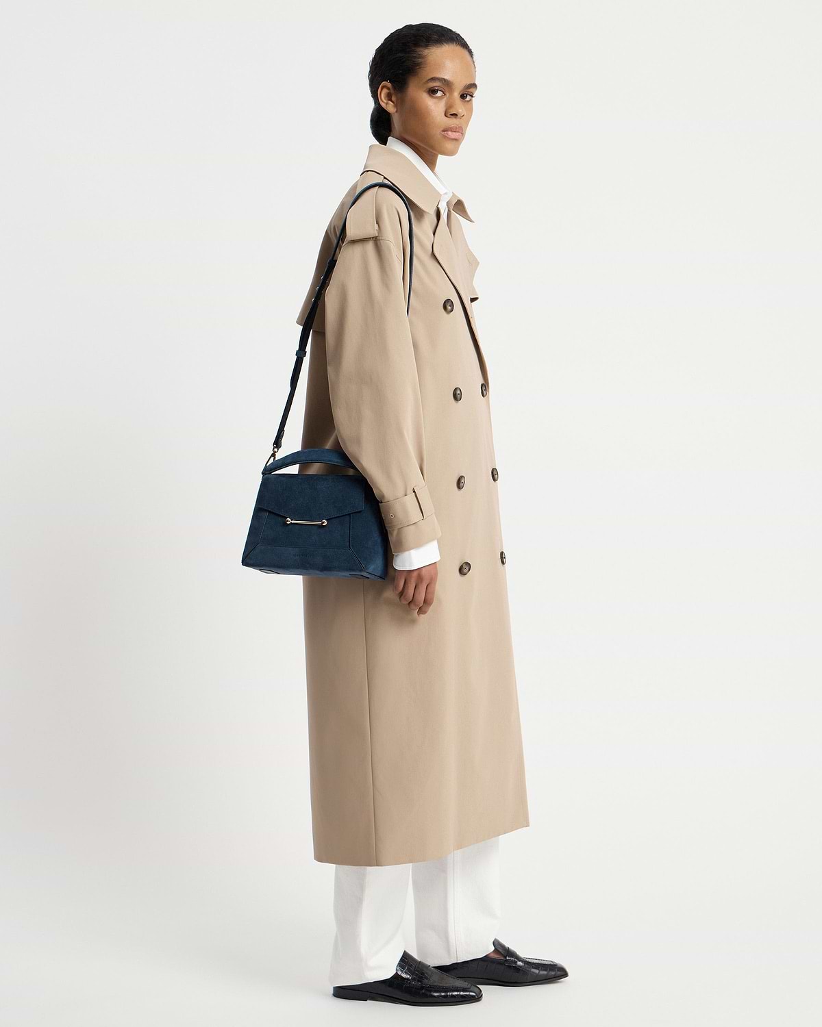 Model wearing beige trench coat carrying a loch blue suede mosaic bag.