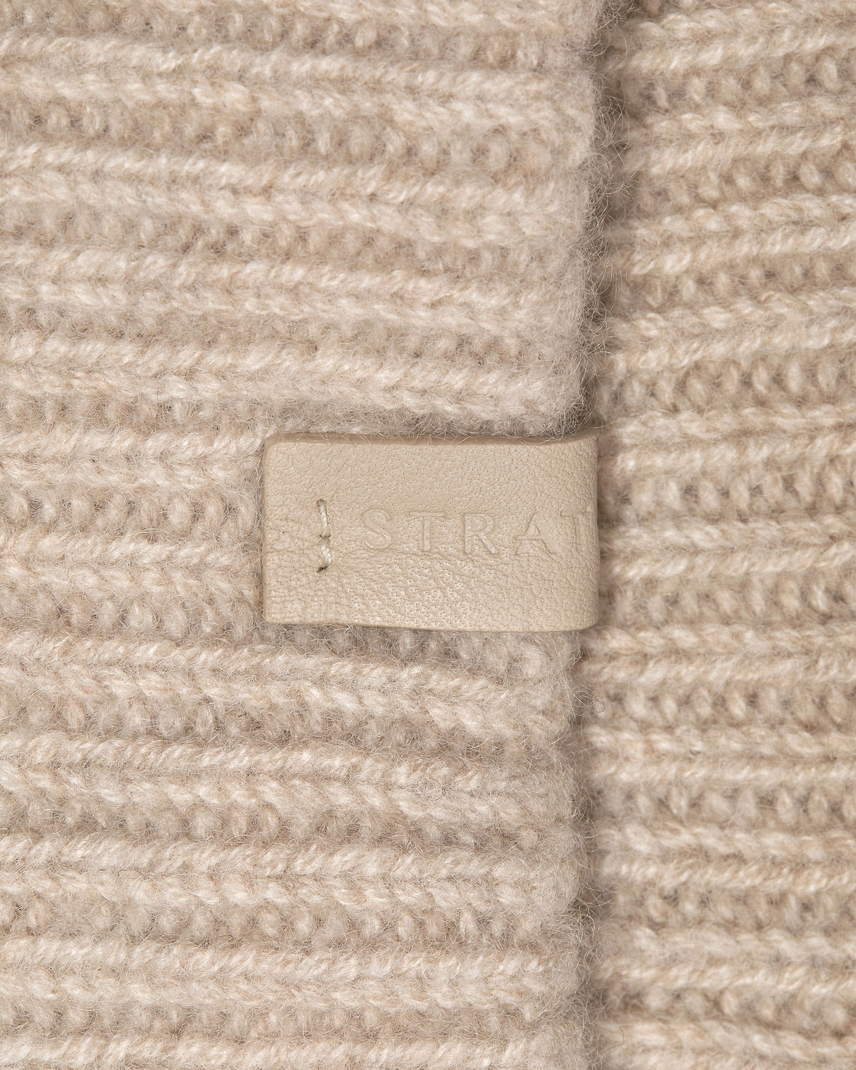 Ribbed oat cashmere headband with leather Strathberry logo tag and visible stitching.