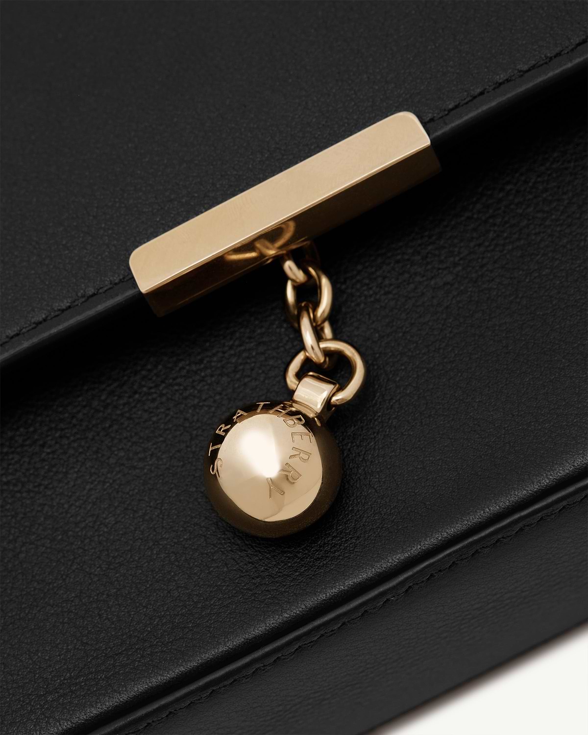 Gold ball charm and chain with Strathberry engraving on black leather clutch