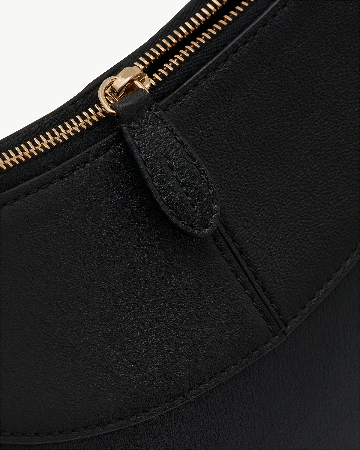Close-up of black leather shoulder bag with gold zip pull and stitched seam.