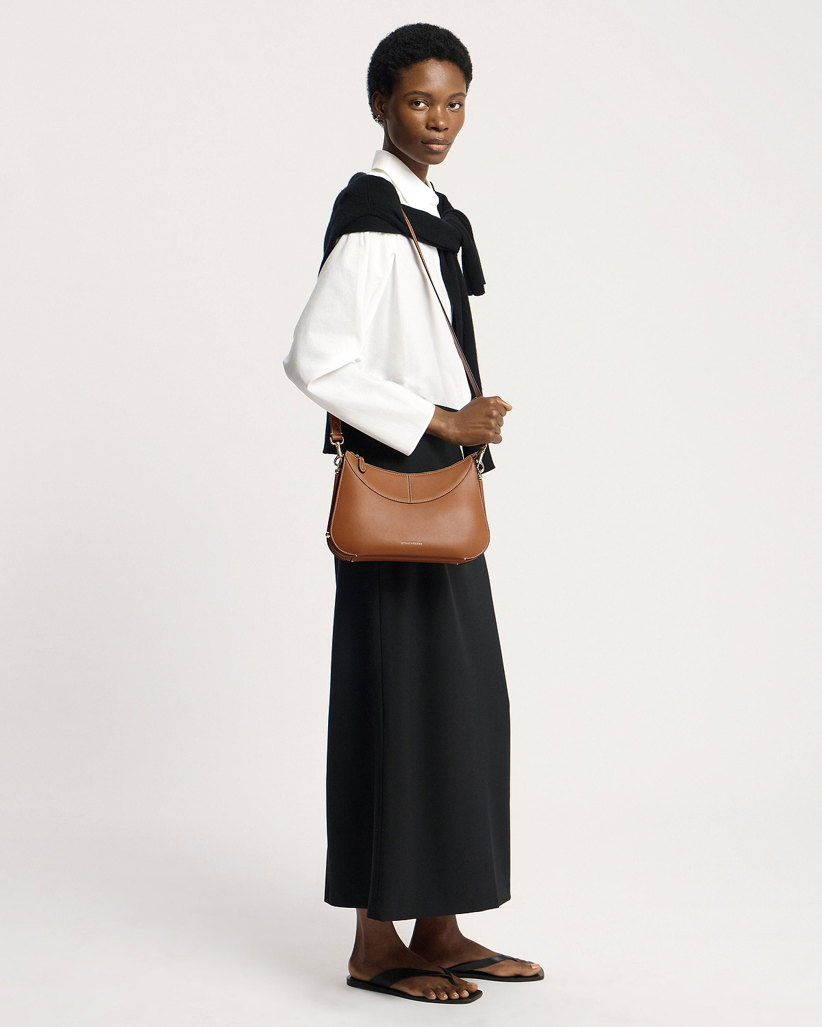 Model wearing tan Nest shoulder bag by Strathberry, crossbody over white shirt.