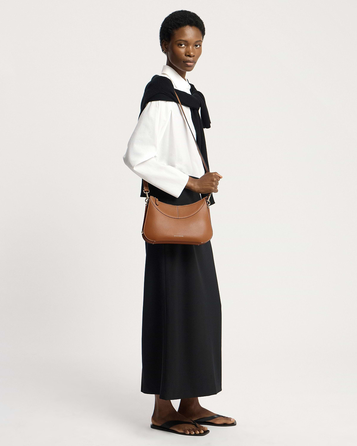 Model wearing tan Nest shoulder bag by Strathberry, crossbody over white shirt.