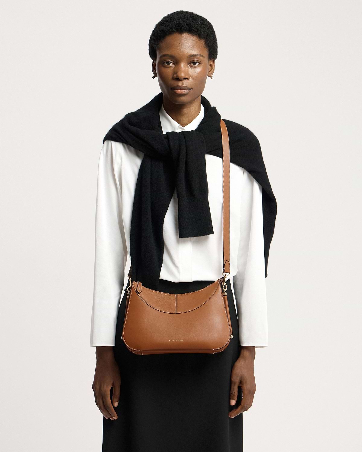 Model wearing tan Nest Shoulder bag worn crossbody over a white shirt.
