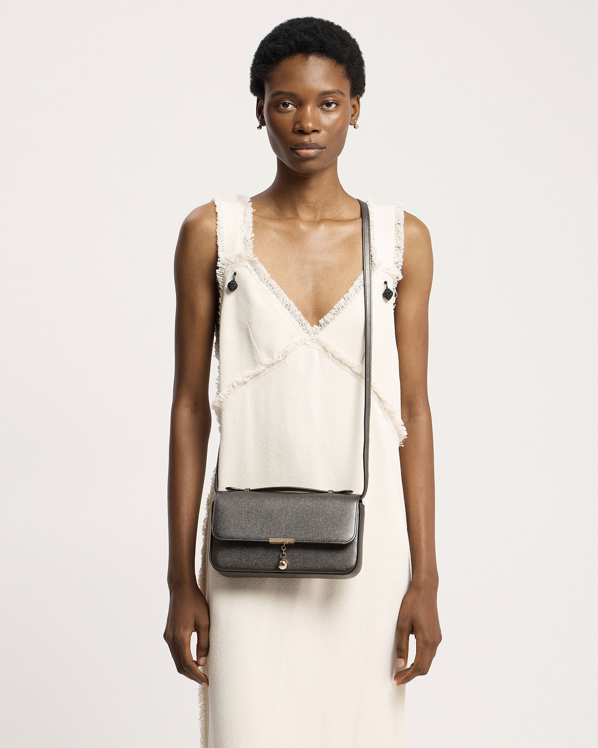 Model wearing white dress carrying metallic anthracite caviar crossbody clutch with gold hardware.