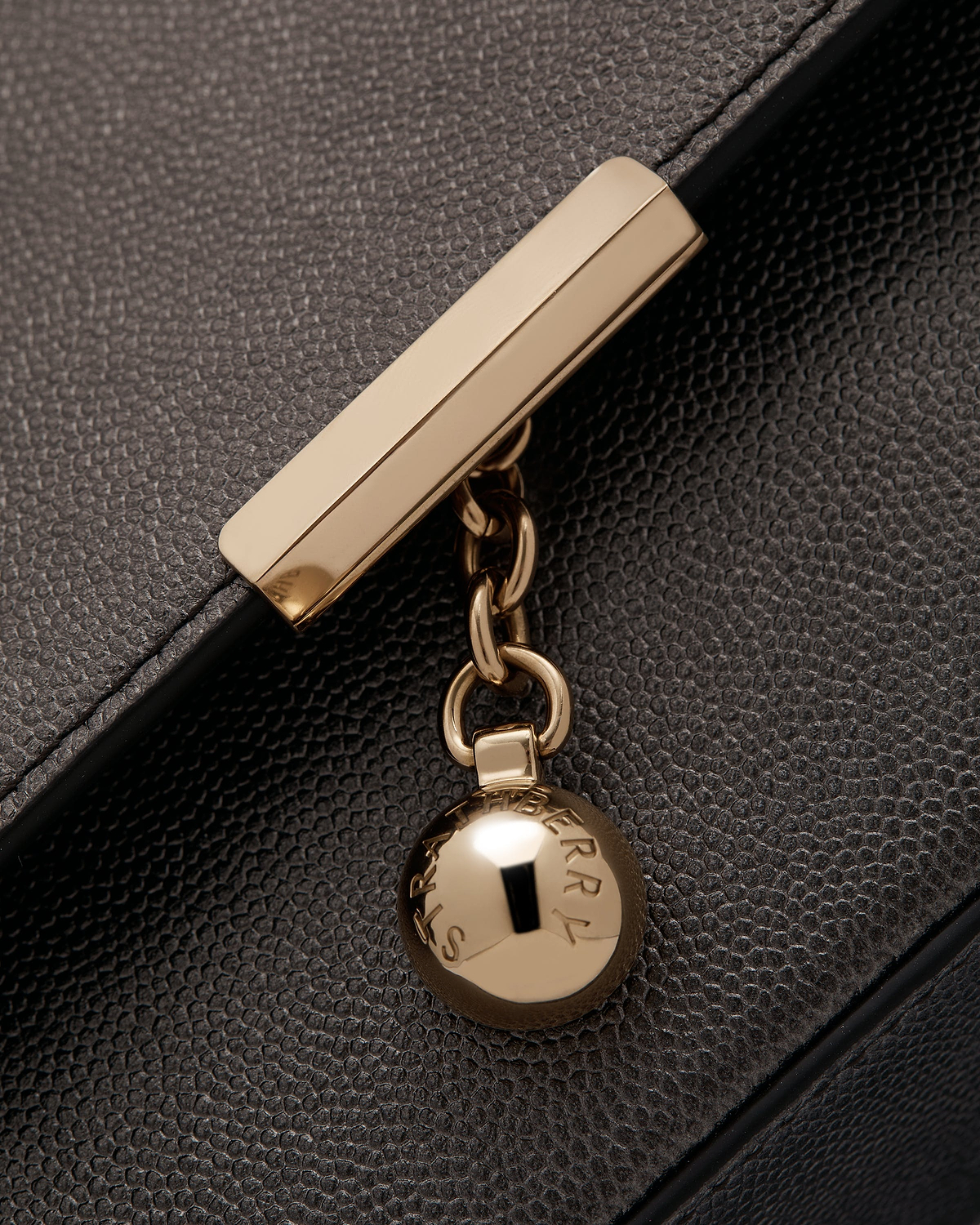 Close up of metallic anthracite caviar leather clutch showing gold bar clasp and Strathberry charm
