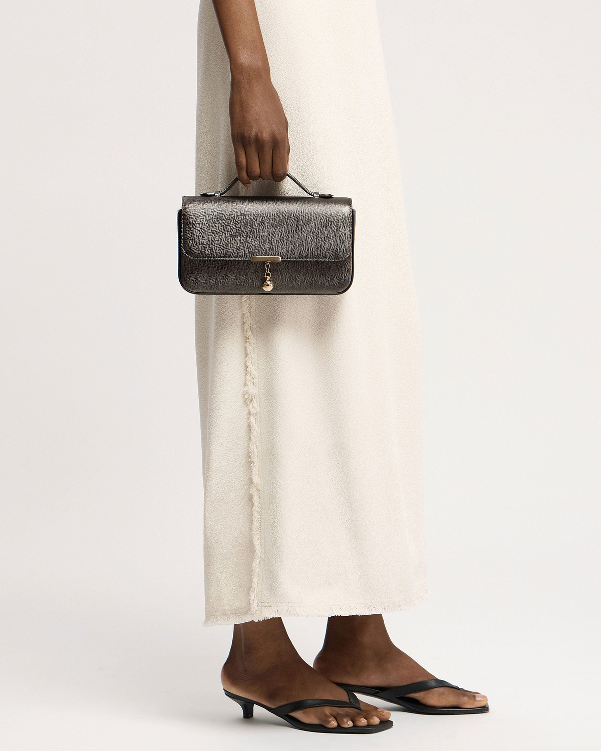 Hand holding metallic anthracite caviar leather clutch with top handle and gold charm.