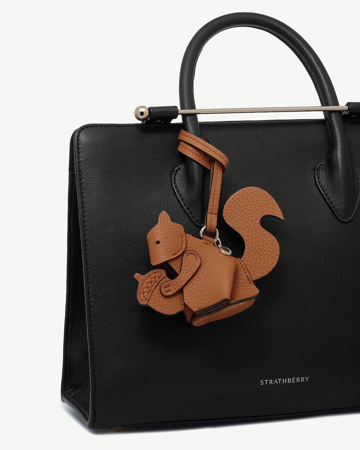 Tan squirrel leather bag charm hanging from black Strathberry tote handle.
