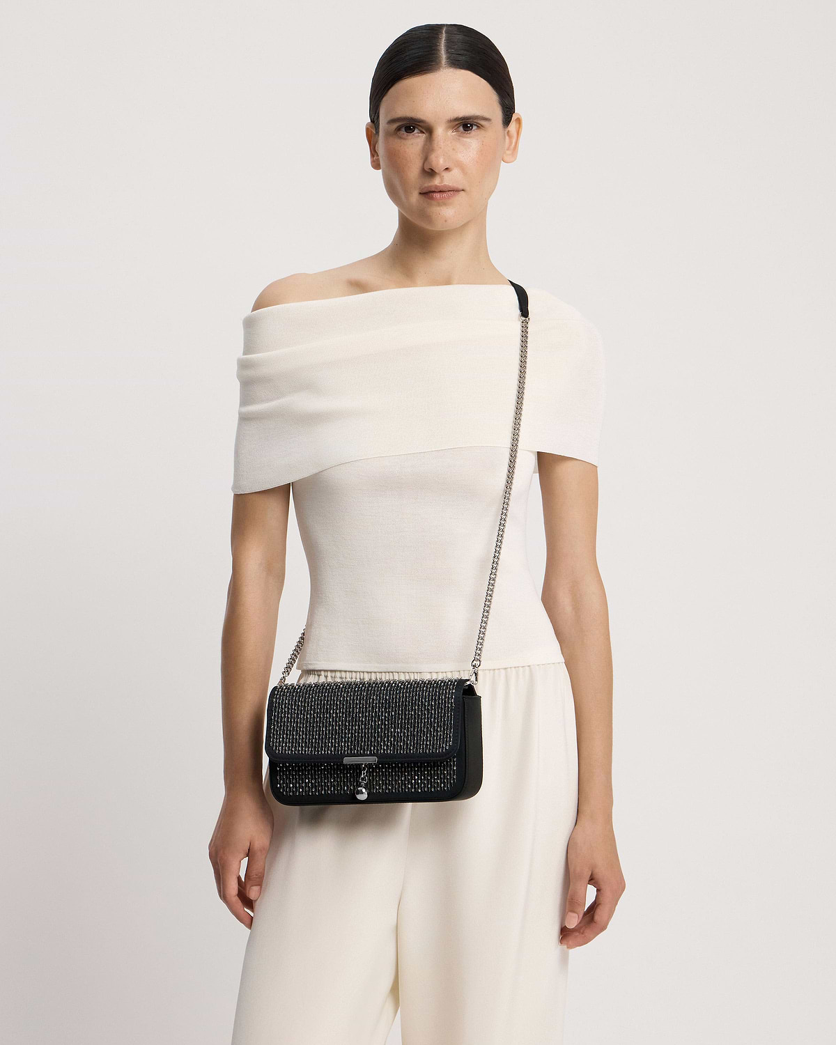 Model wearing black embroidered satin clutch with silver chain strap.