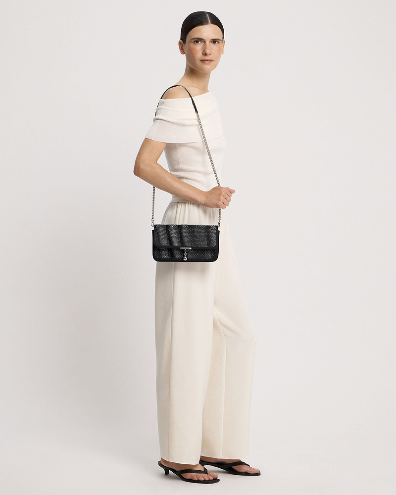 Model wearing a black embroidered satin clutch with a silver chain strap at hip.