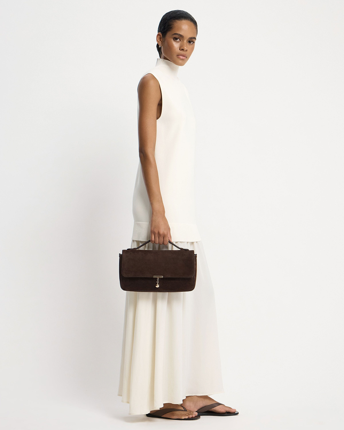 Model holding a Nocturn Midi in espresso suede while wearing a white dress