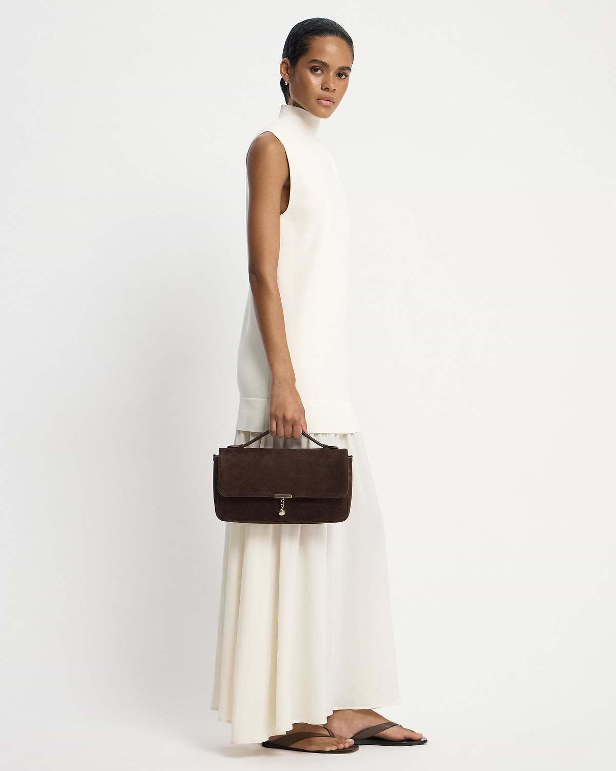 Model holding a Nocturn Midi in espresso suede while wearing a white dress