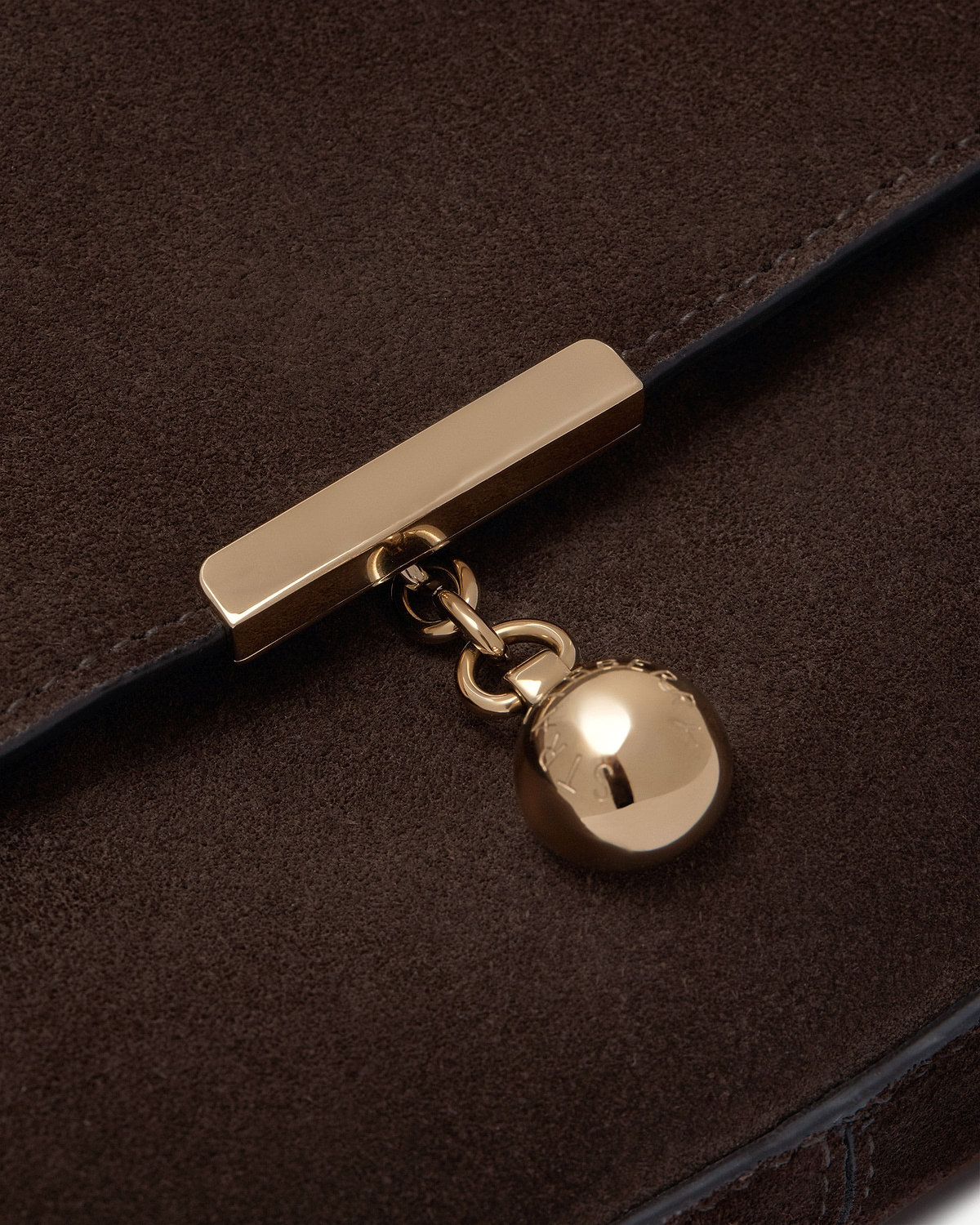 Close-up of espresso suede showing gold bar clasp and round charm.