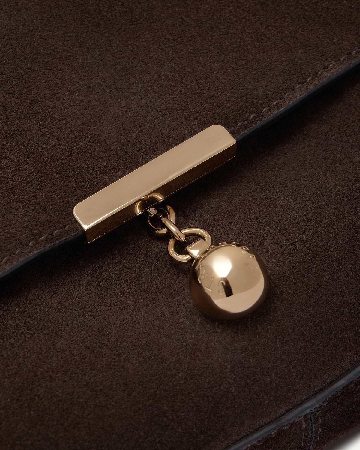 Close-up of espresso suede showing gold bar clasp and round charm.