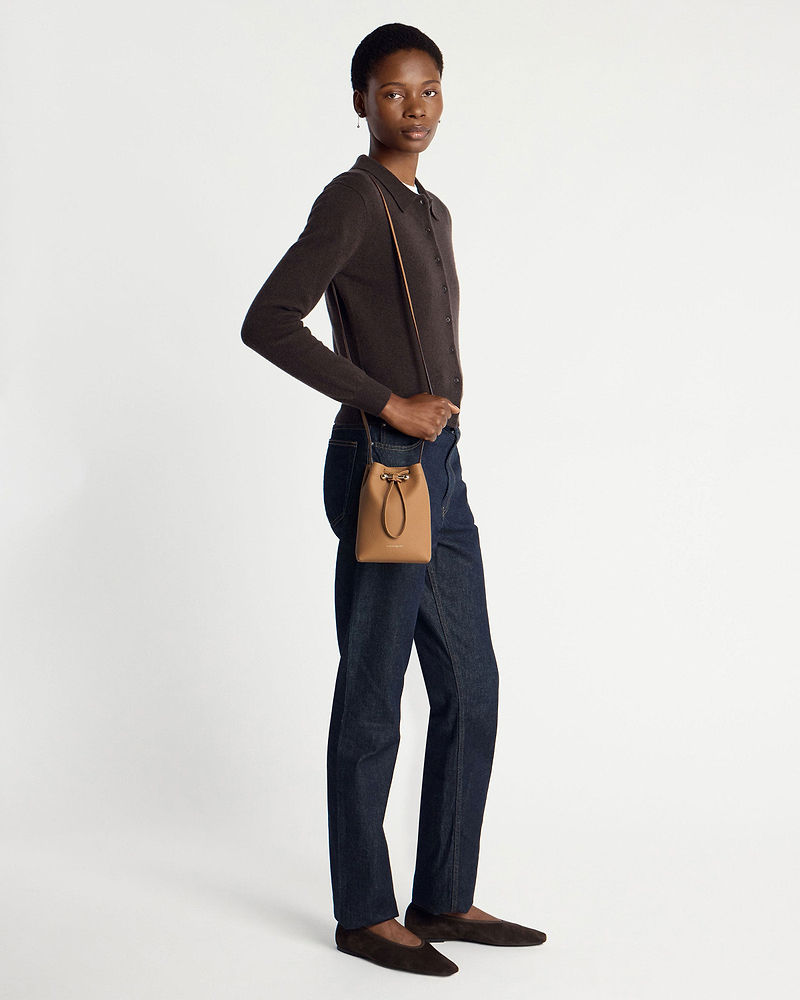 Model wearing caramel midi pouch crossbody with dark cardigan, jeans, brown flats.
