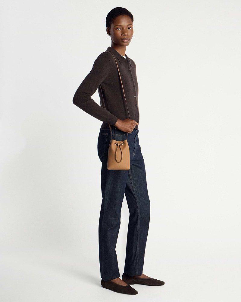 Model wearing caramel midi pouch crossbody with dark cardigan, jeans, brown flats.