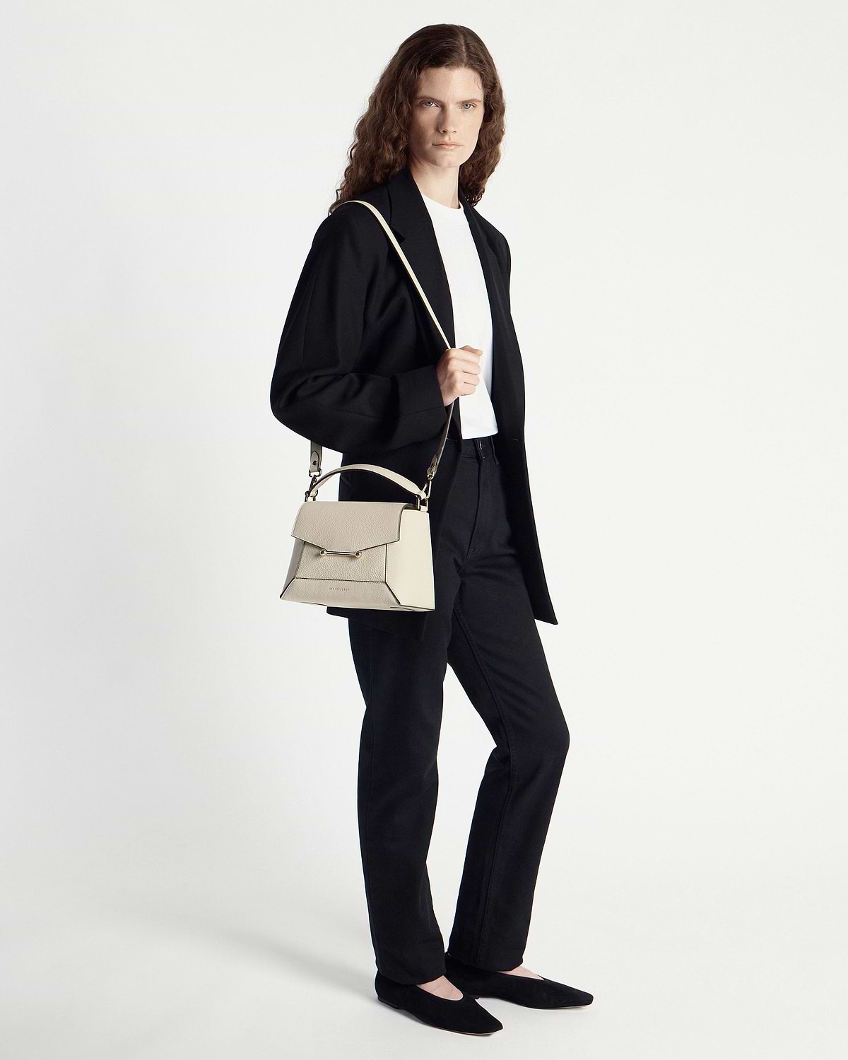 Model in black outfit holding vanilla mosaic bag with top handle and shoulder strap.