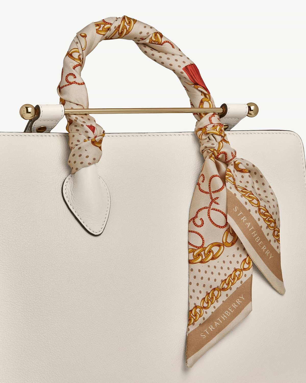 Caramel long silk skinny scarf with diamond chain print tied to bag handle, Strathberry.