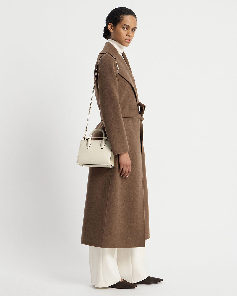 Model wearing a brown coat carrying a vanilla mini tote with chain shoulder strap.