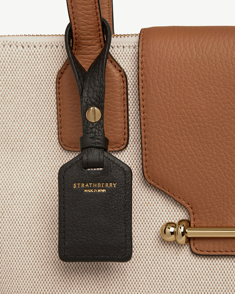 Black leather Strathberry tag on brown leather and canvas bag with gold hardware.