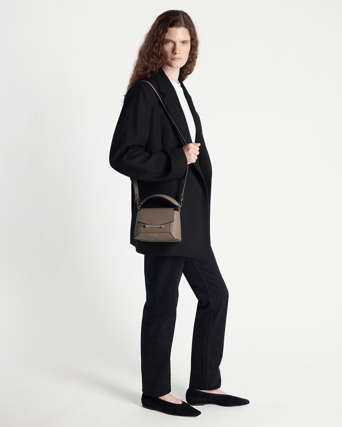 Model wearing a taupe small top-handle crossbody bag over the shoulder.