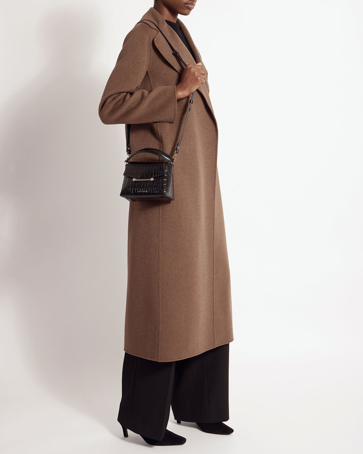 Model in brown coat carrying a soft croc Mosaic Nano crossbody bag.