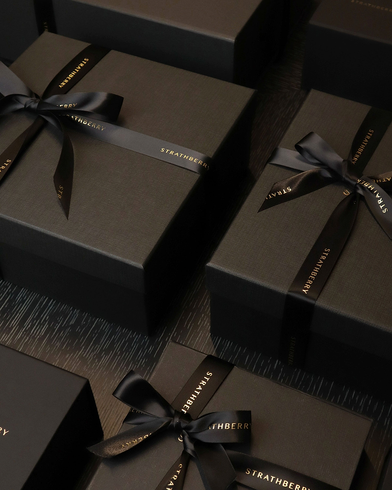 Several black gift boxes tied with black Strathberry ribbons on dark wood