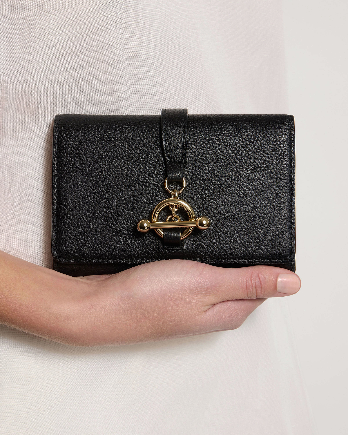Black leather trifold wallet with gold turn-lock, held in one hand.