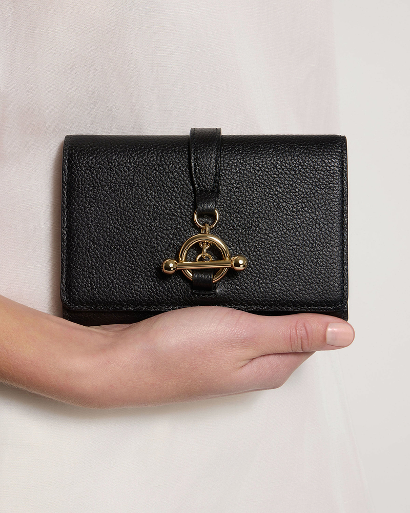 Black leather trifold wallet with gold turn-lock, held in one hand.