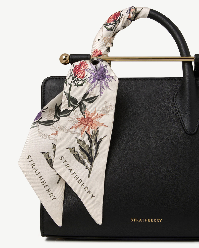 Silk skinny scarf in vanilla with forest green thistle print tied to Strathberry bag.