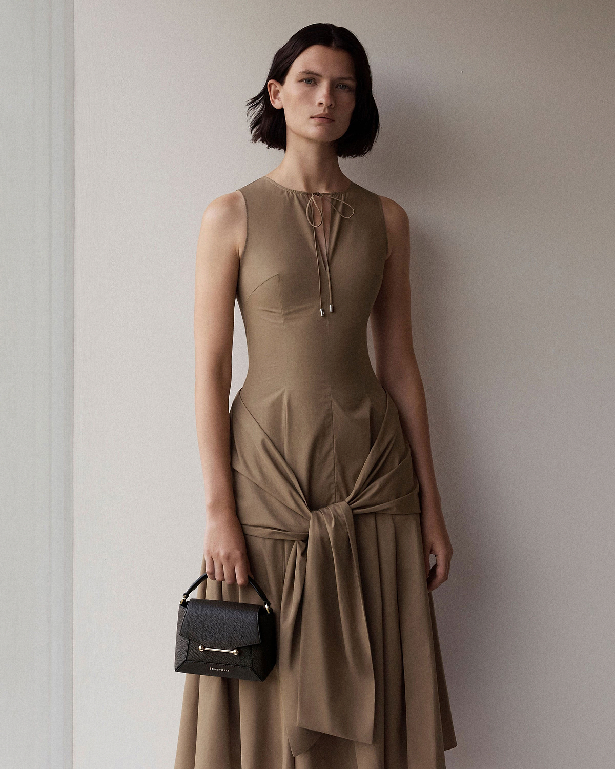 Model holding espresso Mosaic Nano bag by its top handle, Strathberry logo visible.