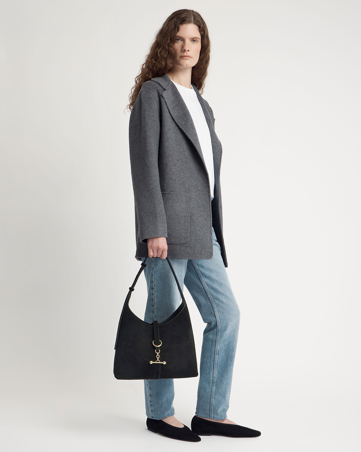 Woman wearing grey coat and jeans holding black suede hobo bag with gold hardware.