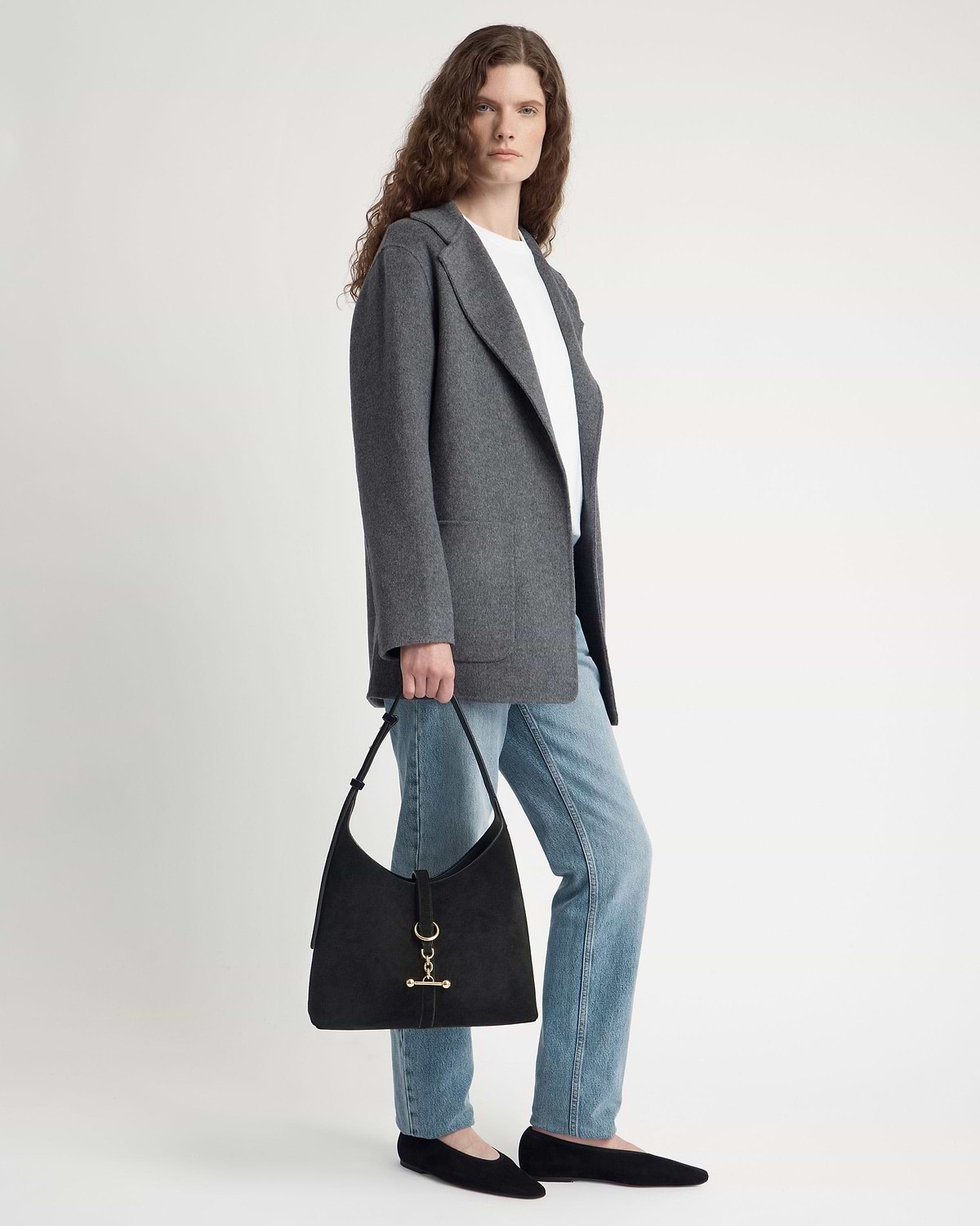 Woman wearing grey coat and jeans holding black suede hobo bag with gold hardware.